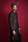 Side profile of Arsalan Iqbal luxury black quilted sherwani with red and silver beadwork, featuring an embroidered mandarin collar and styled with a traditional Ajrak turban against a red background.