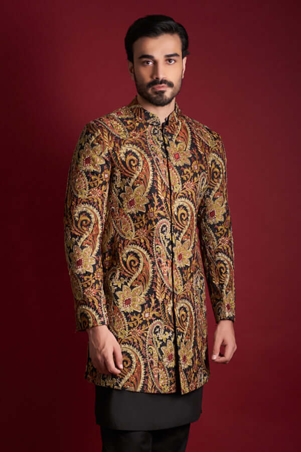 Frontal view of Arsalan Iqbal luxury silk sherwani featuring a multi-colored amber, gold, and red paisley tapestry pattern, styled with a black kurta and mandarin collar.