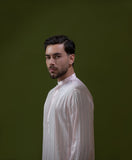 Arsalan Iqbal Blush Pink Chikankari Kurta & Pyjama in Raw Silk Viscose man wearing a light blush pink full sleeve kurta with all-over white chikankari embroidery on raw silk viscose fabric, mandarin collar with button placket, paired with matching white straight-cut pyjama, styled against an olive green wall with a rustic wooden trunk