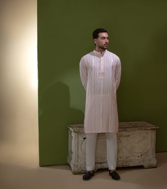 Arsalan Iqbal Blush Pink Chikankari Kurta & Pyjama in Raw Silk Viscose man wearing a light blush pink full sleeve kurta with all-over white chikankari embroidery on raw silk viscose fabric, mandarin collar with button placket, paired with matching white straight-cut pyjama, styled against an olive green wall with a rustic wooden trunk