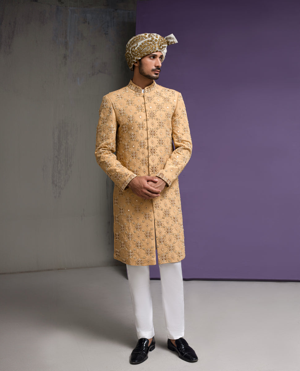 Arsalan Iqbal mustard gold luxury sherwani for men, featuring all-over floral embroidery with mirror-work, paired with a white patterned turban and white formal trousers in a 3/4 front view.