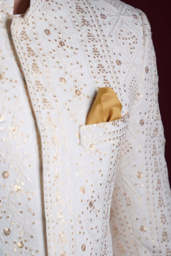 Macro detail of Arsalan Iqbal ivory sherwani featuring vertical gold sequin star patterns, white thread-work embroidery, and a mustard yellow silk pocket square.