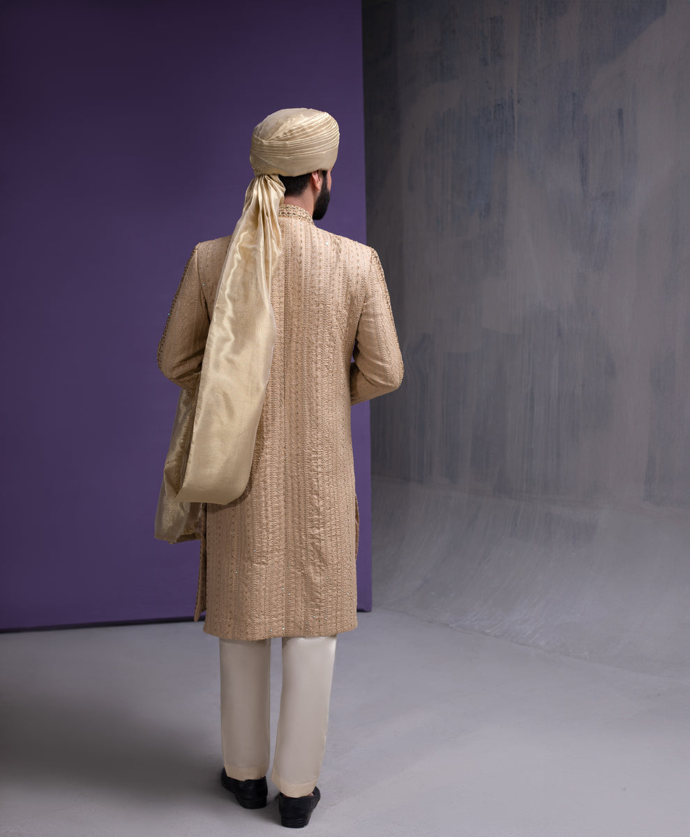 Back view of Arsalan Iqbal gold embroidered sherwani for men, showing the detailed vertical thread work and the elegant drape of a beige silk turban.
