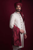 Mid-length portrait of Arsalan Iqbal luxury ivory damask sherwani with a multi-colored paisley embroidered collar, paired with a maroon silk turban and a gold-accented maroon shawl.