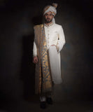 Full-length portrait of Arsalan Iqbal luxury ivory sherwani with diamond-textured fabric, featuring an embroidered mandarin collar, a gold floral silk shawl, matching ivory trousers, and black formal loafers.