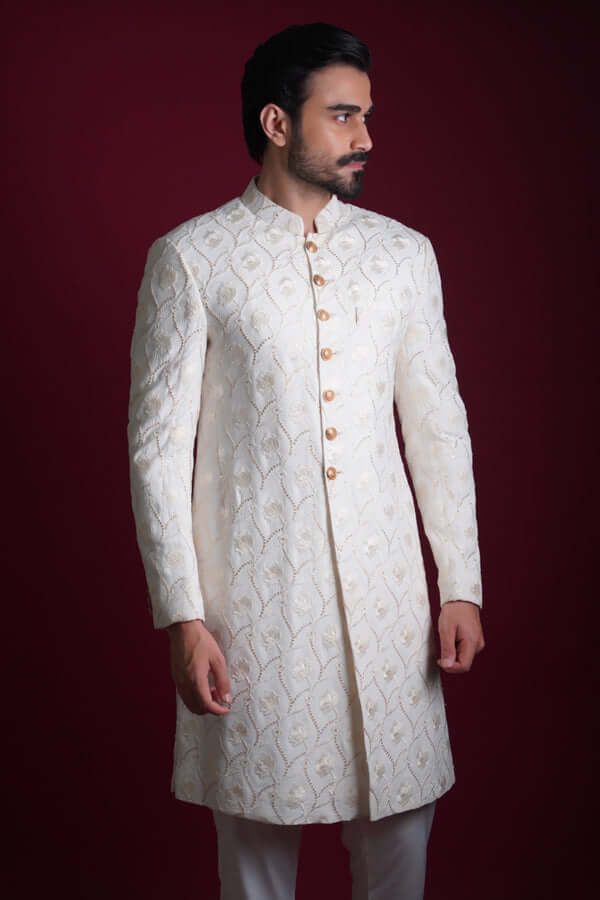 Side profile portrait of Arsalan Iqbal luxury ivory silk sherwani with raised white floral embroidery and gold-toned buttons, showcasing a sharp tailored fit and mandarin collar.