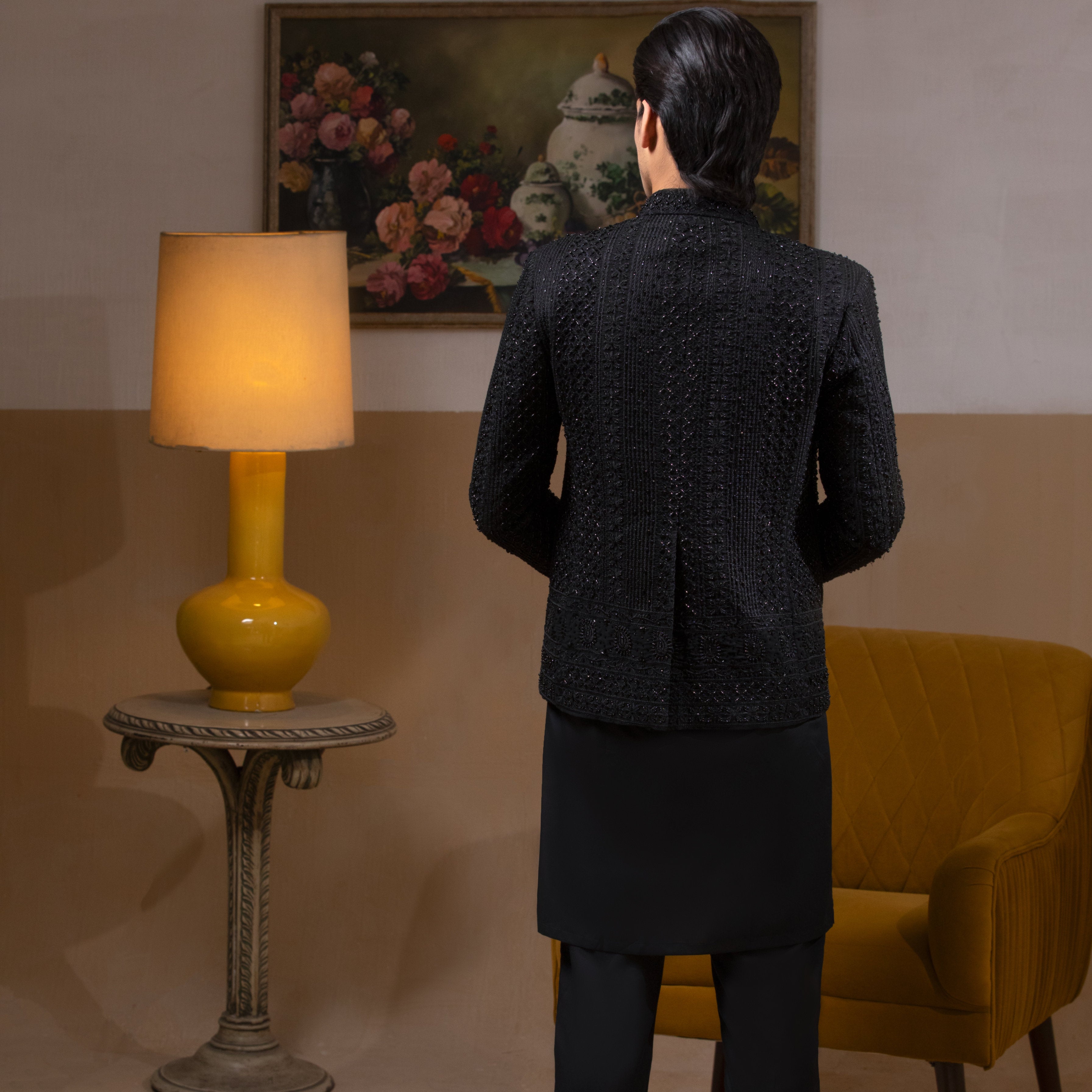 Arsalan Iqbal Jet Black Hand Embroidered Prince Jacket with Kurta Pyjama man wearing a fully embellished jet black prince jacket featuring dense hand embroidery with sequin and thread detailing, paired with a matching black kurta pyjama, mandarin collar, and a sleek formal silhouette, styled in a warm indoor setting