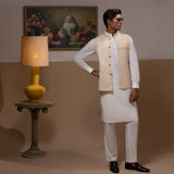 Arsalan Iqbal Light Gold Embroidered Waistcoat with IronEZ Kurta & Pyjama Set man wearing a light gold heavily embroidered sleeveless waistcoat with gold button closure over a crisp white full-sleeve kurta, paired with matching white straight-cut pyjama, accessorized with sunglasses, styled in a warm classic indoor setting