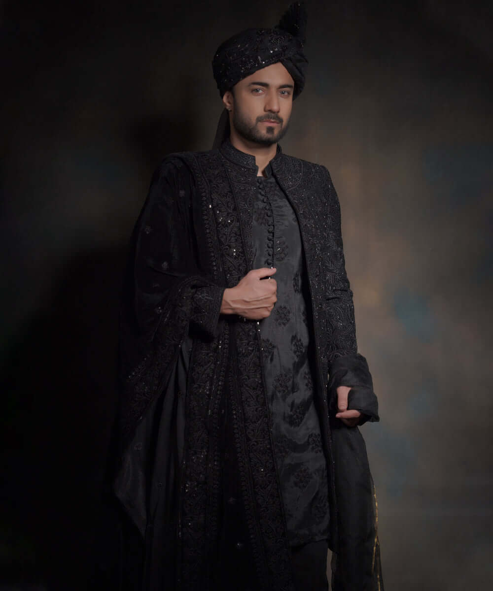 Half-length portrait of Arsalan Iqbal midnight black luxury sherwani, featuring tonal black embroidery and a matching sequined turban with a draped velvet shawl.