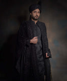 Half-length portrait of Arsalan Iqbal midnight black luxury sherwani, featuring tonal black embroidery and a matching sequined turban with a draped velvet shawl.