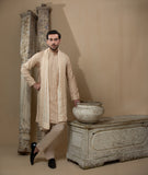 Man wearing Arsalan Iqbal's Peach & Gold Chikankari Kurta Pyjama with a cream stole draped over shoulders, styled with dark formal shoes against a warm beige backdrop