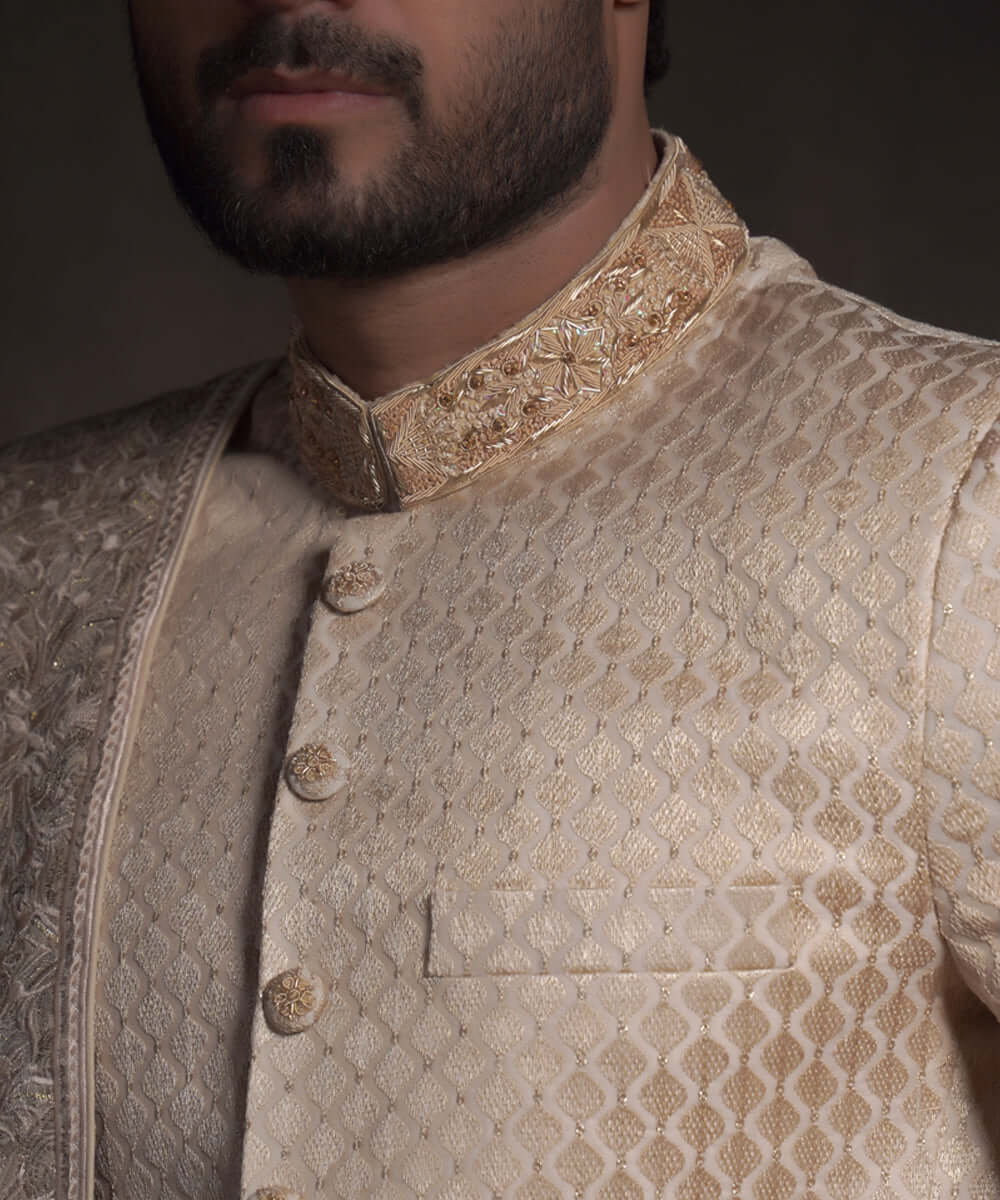 Extreme close-up of Arsalan Iqbal pearl cream sherwani showing the diamond-quilted fabric texture, embroidered mandarin collar with gold threadwork, and matching fabric-covered buttons.