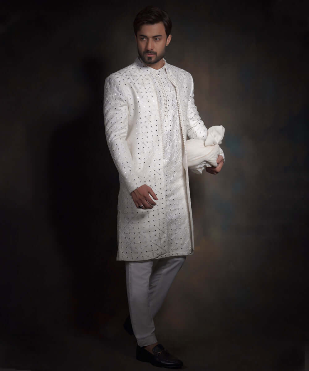 Full-length side view of Arsalan Iqbal snow white luxury sherwani featuring geometric mirror-work, styled with white formal trousers, a matching turban, and black loafers.