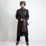 Rear view of an Arsalan Iqbal black velvet sherwani showcasing the tailored silhouette and the long tail of a gold and red dual-tone silk turban.
