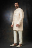 Arsalan Iqbal ivory silk sherwani featuring self-on-self swirl embroidery, gold buttons, and a matching pocket square, paired with cream trousers and embroidered khussas.