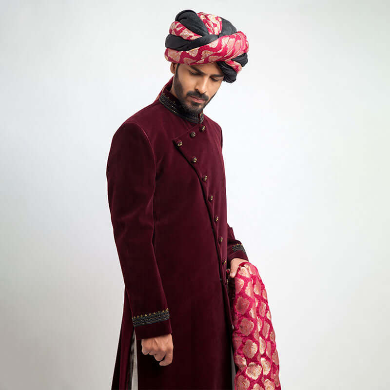 Side view of a man in an Arsalan Iqbal maroon velvet sherwani highlighting the craftsmanship of the cuffs and turban.