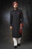 A front-view portrait of a man in a black Arsalan Iqbal embroidered sherwani, featuring a maroon pocket square, maroon and gold turban, and white trousers.