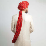 Rear view of an Arsalan Iqbal cream jamawar sherwani showing the tailored fit and the long, draped tail of a vibrant red and gold polka dot silk turban.