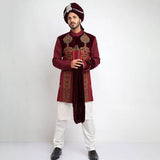 Portrait of a man in an Arsalan Iqbal cream jamawar sherwani with gold embroidered collar and cuffs, paired with a vibrant red and gold polka dot silk turban and matching shawl.