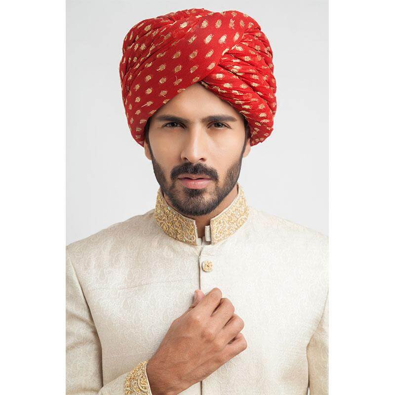 Close-up headshot of an Arsalan Iqbal cream jamawar sherwani with an intricately embroidered gold mandarin collar and a vibrant red and gold polka dot silk turban.