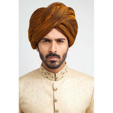 Full-length studio shot of a man in an Arsalan Iqbal gold jamawar sherwani with embroidered collar, mustard yellow pleated turban, and white trousers.