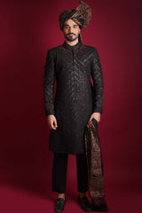 Full-length view of Arsalan Iqbal luxury black sherwani featuring a diamond-quilted pattern and subtle shimmer, styled with a traditional Ajrak print turban and matching Ajrak shawl, paired with black trousers and formal loafers.