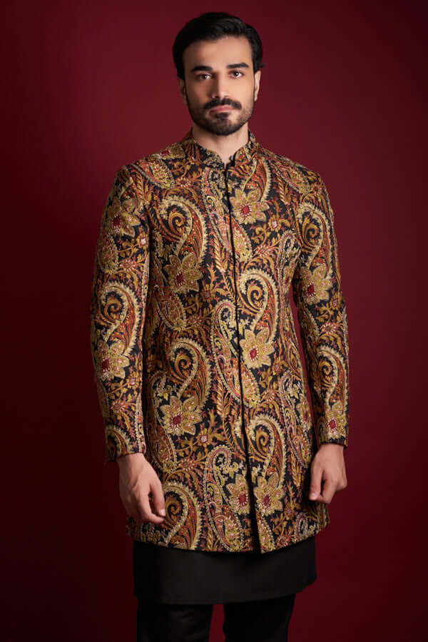 Front-facing view of Arsalan Iqbal luxury short-length silk sherwani featuring a multi-colored amber, gold, and red paisley tapestry print with a mandarin collar, paired with black trousers.