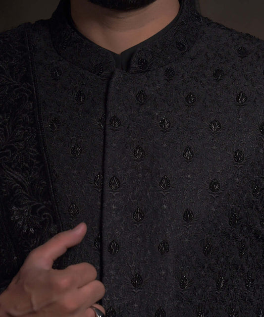 Close-up of Arsalan Iqbal midnight black sherwani featuring spaced-out tonal floral motifs, intricate hand-embroidery with black beads, and a mandarin collar.