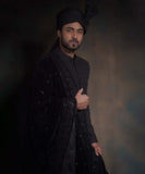 Portrait of Arsalan Iqbal midnight black sherwani with spaced-out tonal floral motifs, featuring a draped velvet shawl with heavy embroidery and a matching high-pleated turban.