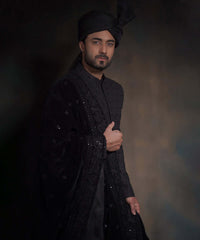 Portrait of Arsalan Iqbal midnight black sherwani with spaced-out tonal floral motifs, featuring a draped velvet shawl with heavy embroidery and a matching high-pleated turban.
