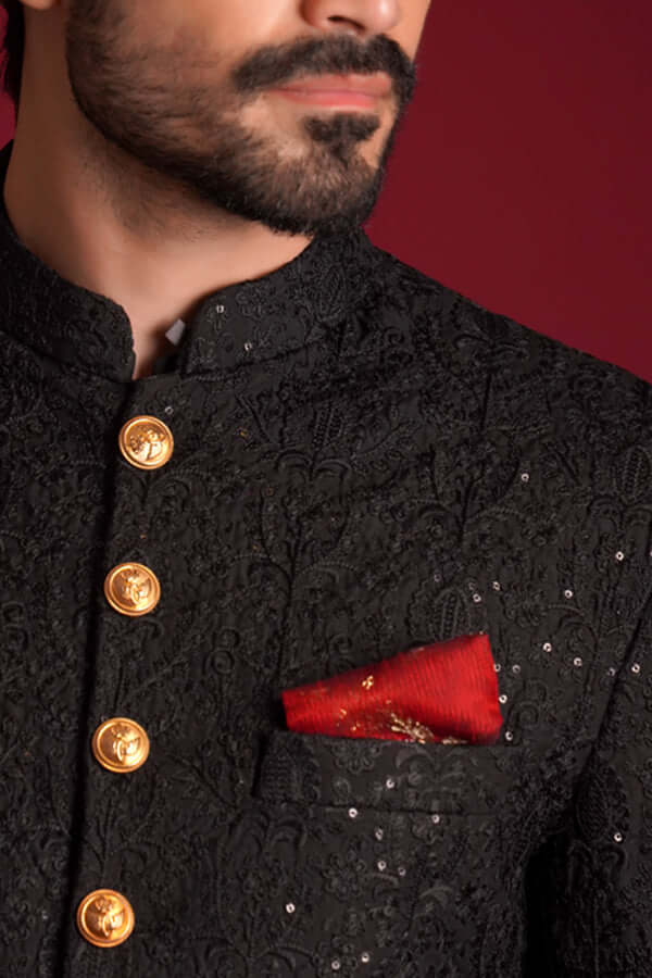 Extreme close-up of Arsalan Iqbal luxury black sherwani featuring tonal floral embroidery with silver sequins, decorative gold embossed buttons, and a textured red silk pocket square.