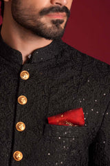 Extreme close-up of Arsalan Iqbal luxury black sherwani featuring tonal floral embroidery with silver sequins, decorative gold embossed buttons, and a textured red silk pocket square.