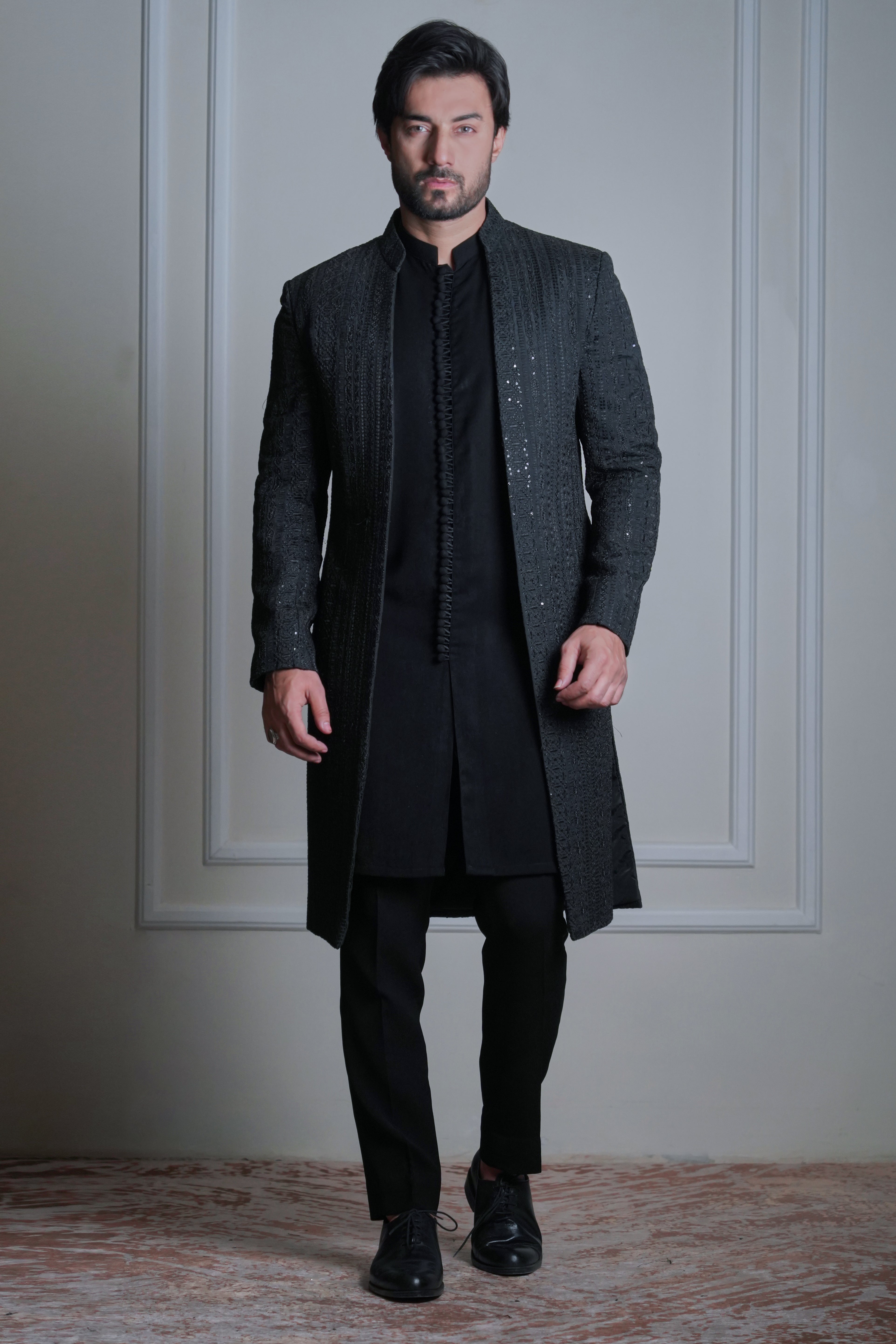 Male model wearing a black sherwani by Arsalan Iqbal, modern formal ethnic menswear in an elegant indoor setting