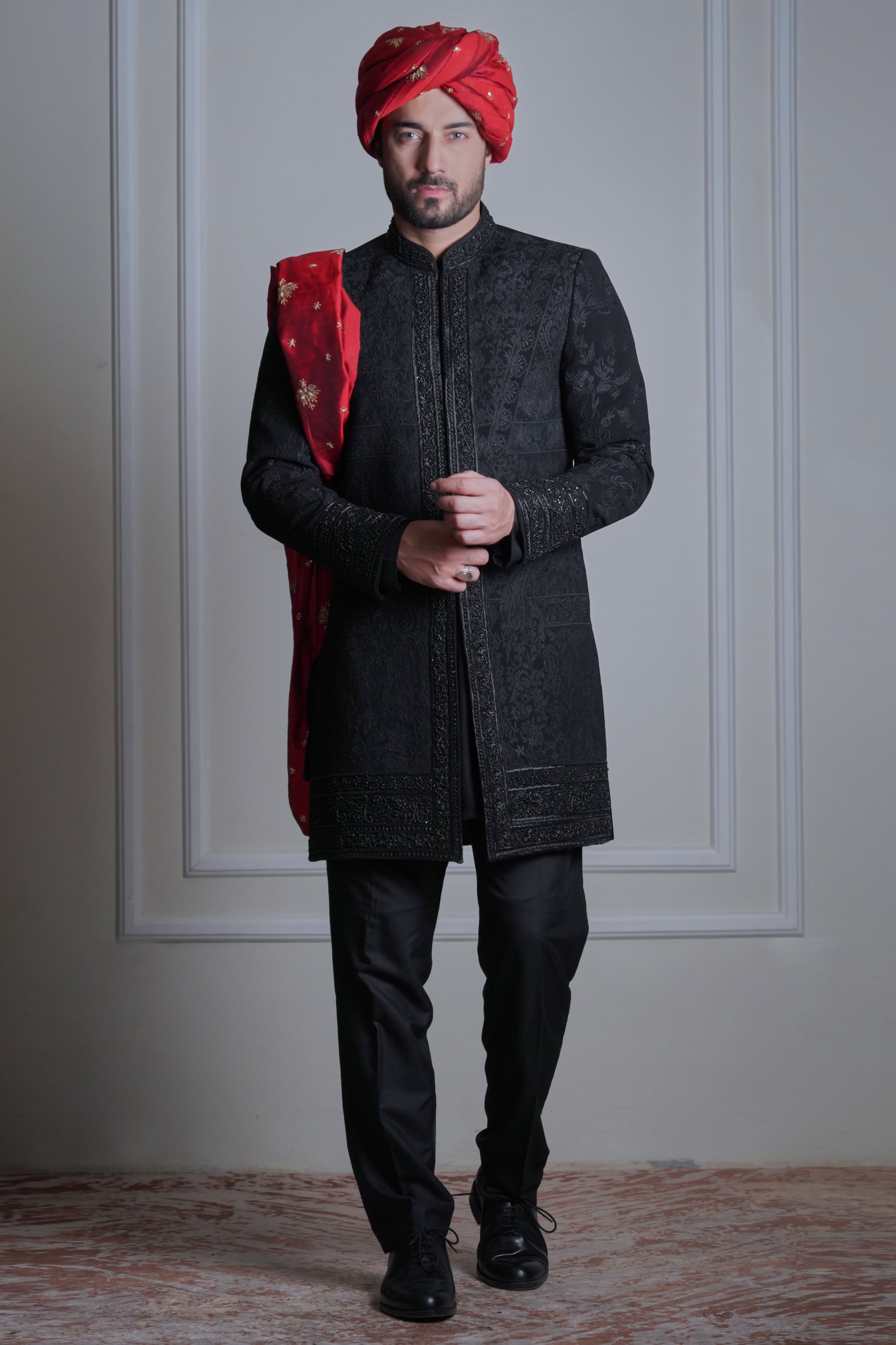 Male model wearing a black sherwani with red turban by Arsalan Iqbal, luxury South Asian groom wedding attire