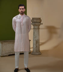 Arsalan Iqbal Blush Pink Chikankari Kurta & Pyjama in Raw Silk Viscose – man wearing a light blush pink full-sleeve kurta with all-over white chikankari embroidery on raw silk viscose fabric, mandarin collar with button placket, paired with matching white straight-cut pyjama, styled against an olive green wall with a rustic wooden trunk