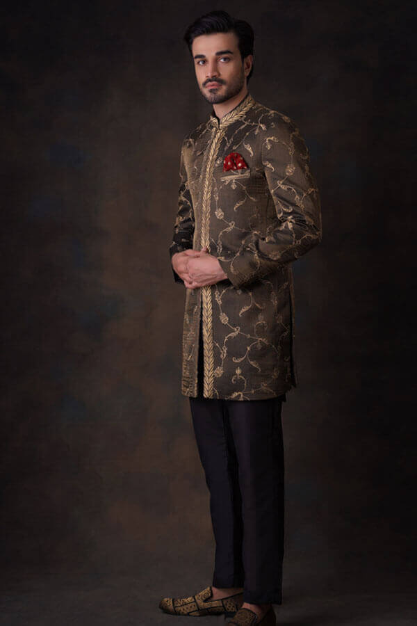 Side-profile view of Arsalan Iqbal luxury bronze-olive sherwani with gold ivy vine embroidery, featuring a gold leaf patterned placket, a red pocket square, and embellished loafers.