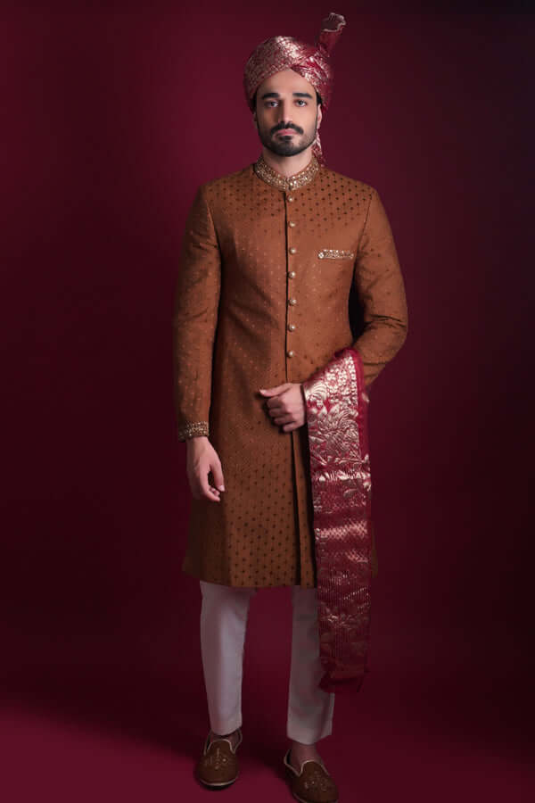 Arsalan Iqbal luxury copper-brown sherwani with black geometric micro-motifs, featuring a gold-embroidered mandarin collar and cuffs, paired with a maroon Banarasi shawl and turban.