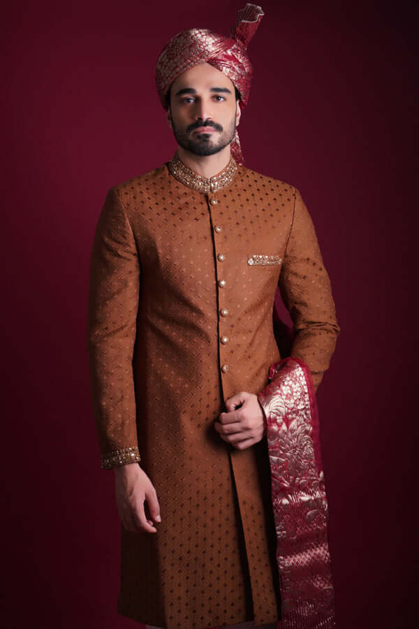 Arsalan Iqbal copper-brown sherwani with black geometric motifs, featuring a gold-studded mandarin collar, maroon Banarasi shawl, and a matching silk turban.