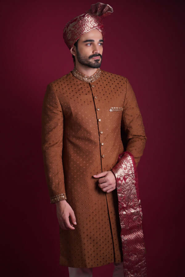Arsalan Iqbal copper-brown sherwani with black geometric motifs, featuring a gold-studded collar, maroon Banarasi shawl, and matching turban.