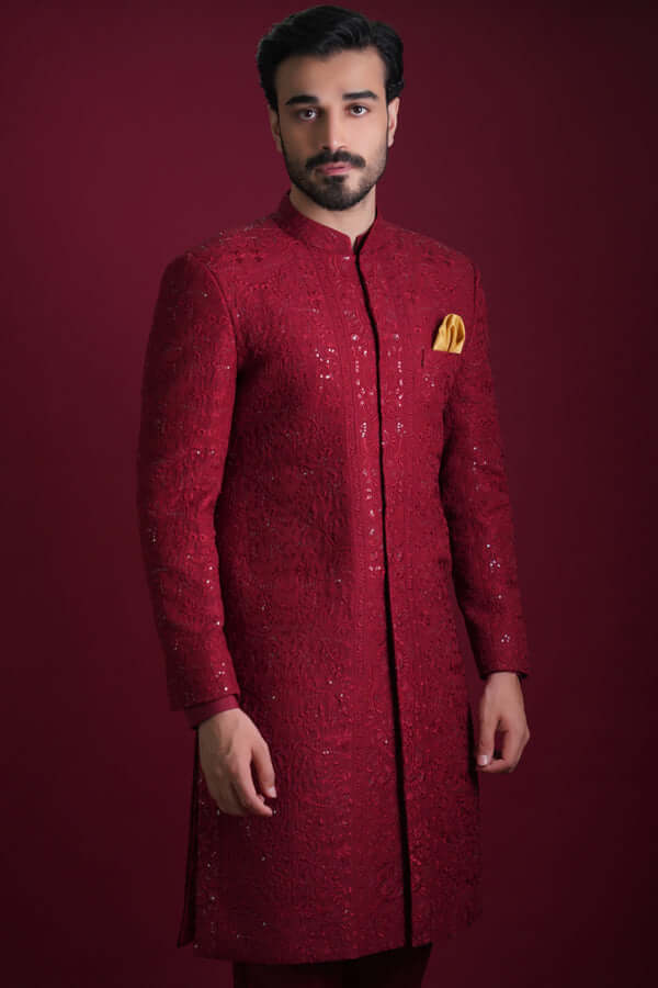 Arsalan Iqbal luxury crimson red sherwani featuring dense tonal floral embroidery, silver sequin accents, and a mustard yellow silk pocket square.