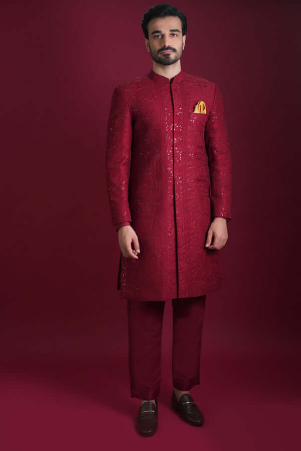 Arsalan Iqbal luxury crimson red sherwani with tonal geometric embroidery and silver sequin accents, featuring a mustard silk pocket square and matching red trousers.