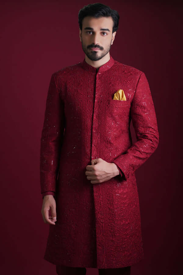 Arsalan Iqbal luxury crimson red sherwani with tonal floral embroidery, silver sequins, and a mustard silk pocket square, featuring a model holding the front placket.