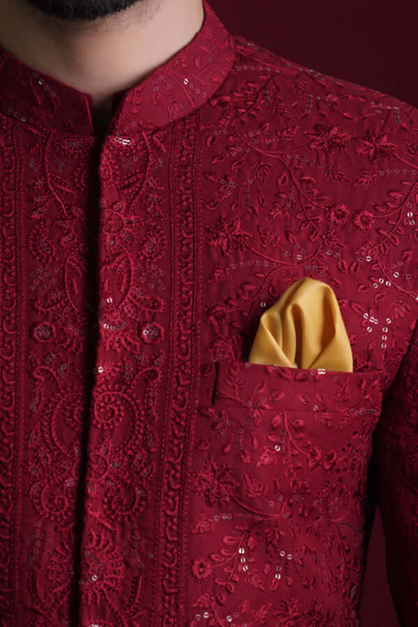 Macro detail of Arsalan Iqbal crimson red sherwani featuring intricate tone-on-tone floral thread-work, silver reflective sequins, and a mustard silk pocket square.