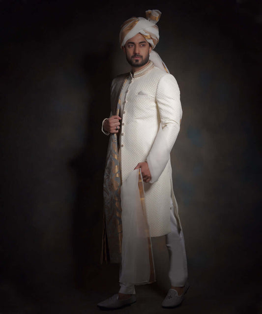 Arsalan Iqbal luxury ivory sherwani with a subtle diamond-textured fabric, featuring an embroidered mandarin collar, styled with a gold and white patterned turban, a matching pocket square, and white formal trousers.