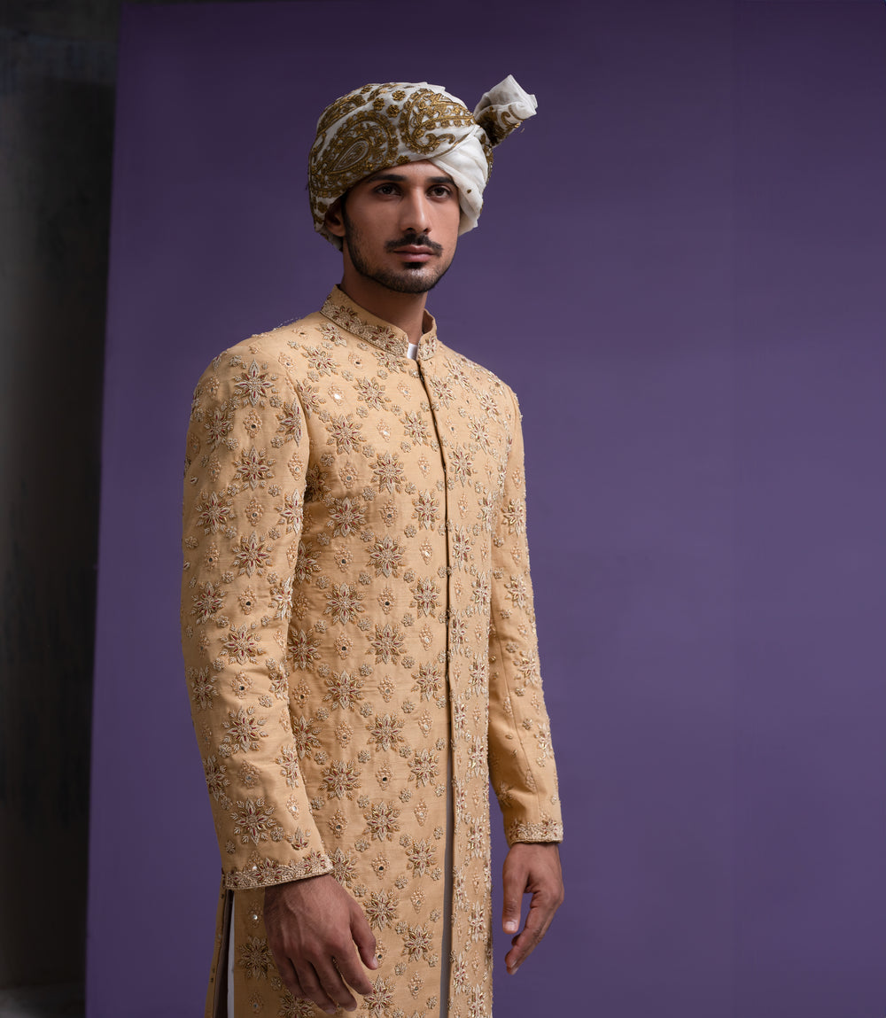 Front side view of Arsalan Iqbal mustard gold floral embroidered sherwani for grooms, featuring mirror-work highlights, a traditional patterned turban, and white formal trousers.
