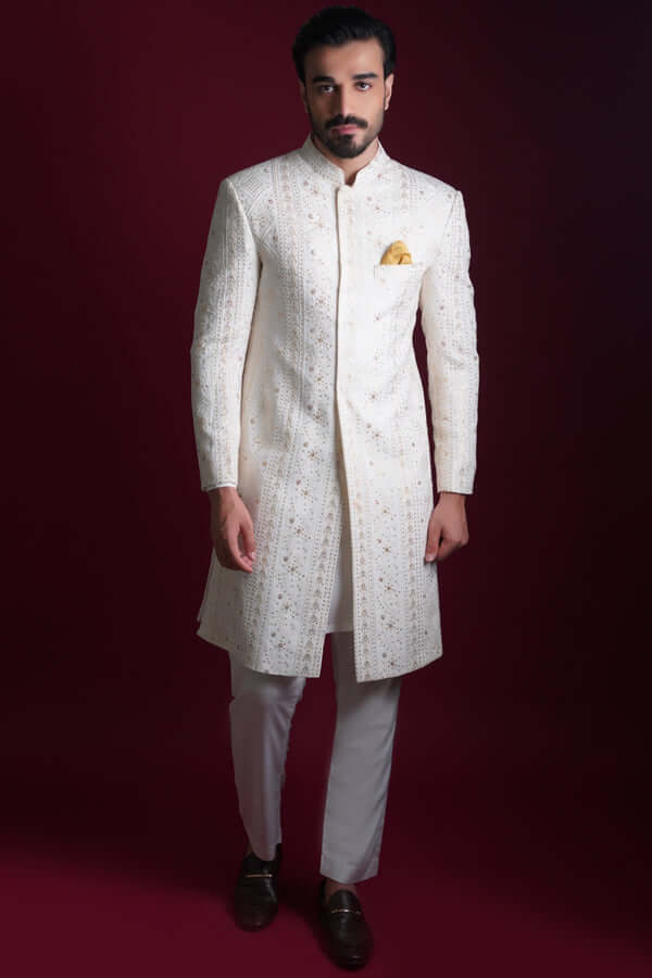 Full-length view of Arsalan Iqbal luxury ivory sherwani featuring vertical geometric and star-shaped gold embroidery, a mandarin collar, and a yellow silk pocket square, paired with white trousers.
