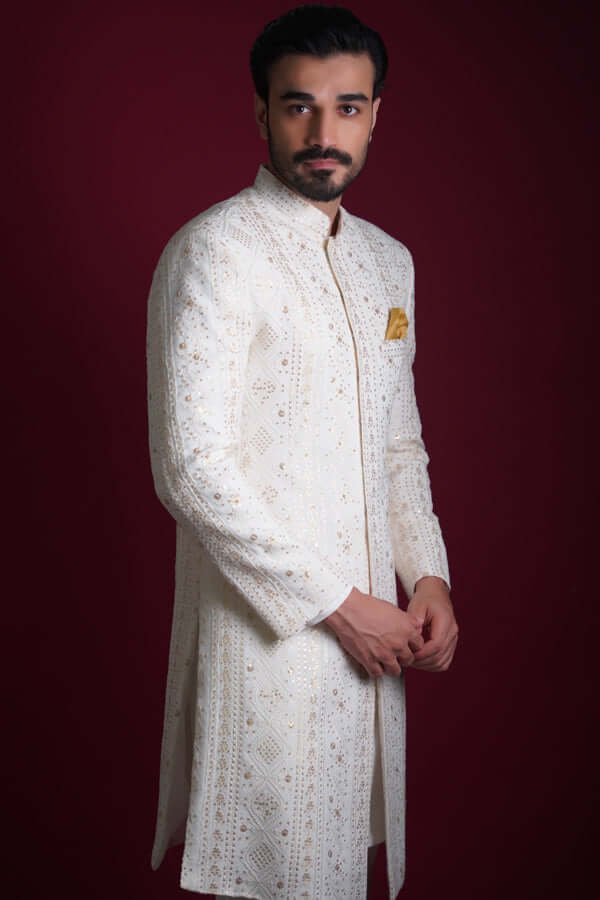 Side profile portrait of Arsalan Iqbal luxury ivory sherwani with vertical gold geometric star embroidery, featuring a mustard silk pocket square and a sharp structured fit.