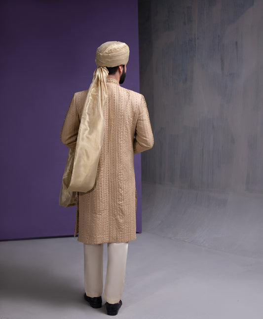 Back view of Arsalan Iqbal gold embroidered sherwani for men, showing the detailed vertical thread work and the elegant drape of a beige silk turban.