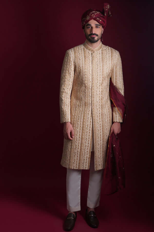 Arsalan Iqbal cream and gold sherwani with architectural chevron embroidery, paired with white trousers and a maroon embroidered turban and shawl.