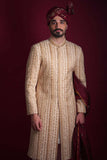 Arsalan Iqbal luxury cream and gold sherwani featuring vertical chevron embroidery and floral panels, paired with a maroon embroidered turban and shawl.